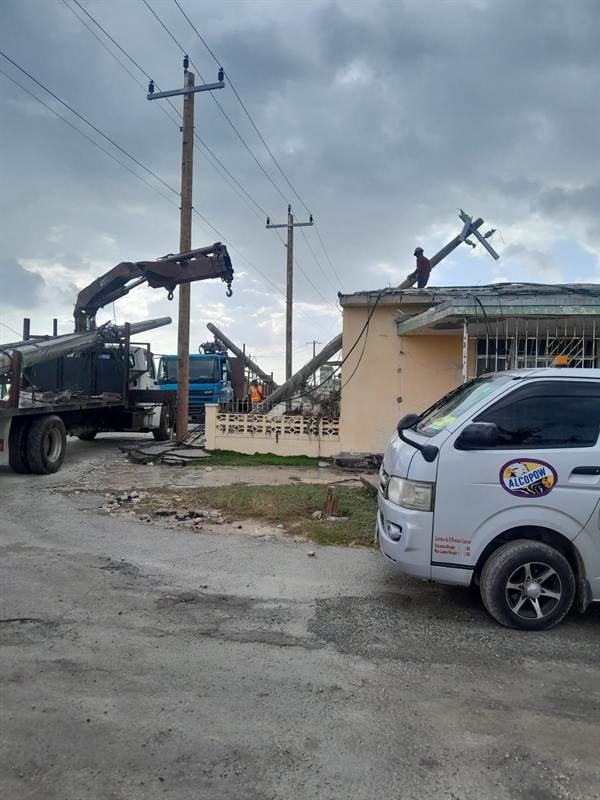 Alcopow crane truck and crew clearing a downed pole leaning on a rooftop during Hurricane Melissa restoration